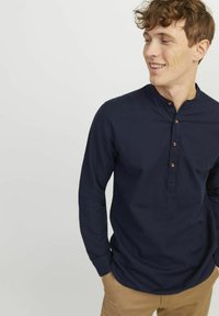 Camicia a maniche lunghe blu navy in un materiale leggero, con colletto alla coreana e quattro bottoni in legno lungo la patta.