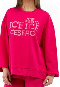 Felpa over-size fucsia con una texture morbida, con una grafica audace in bianco con il testo "ICE ICEBERG" in stili differenti sul davanti.