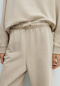 Beige huppari ja sweatsuit, jossa on kiristysvyötärö, ribattu hihansuu ja pehmeä, teksturoitu kangas. Molemmilla osilla on rento istuvuus.