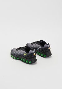 Sapatilhas atléticas pretas e cinzas com detalhes em verde na sola em bolha, parte superior texturizada e um logótipo swoosh distinto. Design com atacadores, suporte de amortecimento.