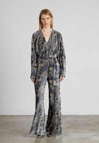 Mono con estampado floral que presenta mangas largas, un escote en V profundo y una cintura ceñida con cinturón. Confeccionado con una tela texturizada en tonos azul oscuro y beige.