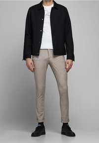 Svart knäppjacka över en vit skjorta, tillsammans med beige rutiga byxor och svarta sneakers. Materialet verkar slätt; designen är skräddarsydd.