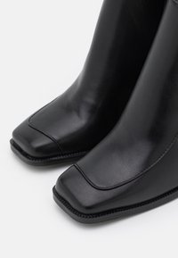 Botas de tornozelo em couro preto com um design de bico quadrado, textura suave e costura em contraste ao longo da sola.