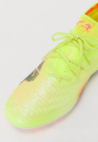 Lys gul fotballsko med teksturert overflate, levende rosa detaljer og mønstrete lisser. Har en tettsittende passform og lett design.