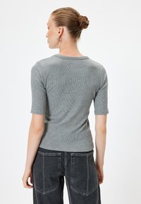 Grijze geribbelde top met korte mouwen en een ronde hals, gecombineerd met hoge zwarte denimjeans met achterzakken.