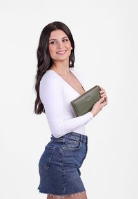 Green leather wallet held by a person, featuring a zip closure and decorative stitching, against a plain white background.