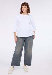 Top in cotone bianco con maniche 3/4 e decorazioni colorate disperse. Abbinato a jeans in denim chiaro a gamba larga e sneakers bianche.