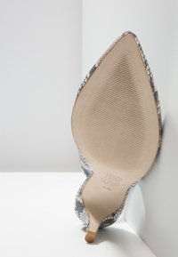 Scarpa con tacco alto e punta affusolata, realizzata in pelle con stampa rettile blu e grigia. La suola è liscia con dettagli rigati per una migliore aderenza.