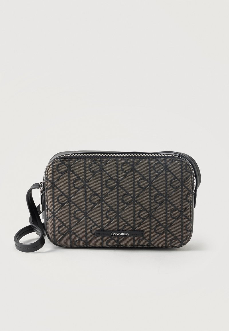 Ορθογώνια τσάντα Calvin Klein crossbody με μαύρο μοτίβο λογότυπου, μαύρο φερμουάρ και ρυθμιζόμενο μαύρο λουράκι σε λευκό φόντο.