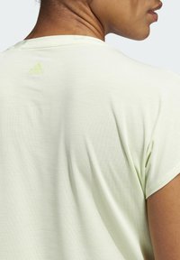 Jasnozielona koszulka wykonana z miękkiego materiału, z okrągłym dekoltem i krótkimi rękawami. Na plecach znajduje się logo Adidas wydrukowane w jaśniejszym odcieniu.