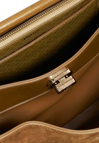 Tan suede handbag with a gold zip closure, featuring a textured light green lining and a silver clasp. Smooth, clean interior design.