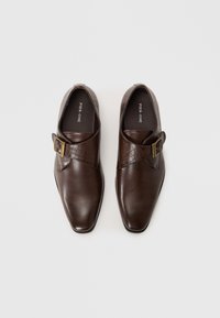 Zapatos de cuero marrón con forma de punta, presentando un patrón texturizado de cocodrilo y un detalle de hebilla lateral. Acabado suave en general.