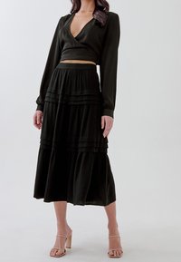 Top nero corto a portafoglio con maniche lunghe abbinato a una gonna nera a balze, fluida. Tessuto liscio, con pieghe orizzontali sulla gonna.