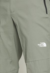 Jasnozielone spodnie techniczne o gładkiej teksturze, z boczną kieszenią i białym logo The North Face na dolnej części nogawki.