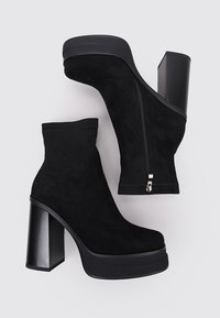 Botines de ante negro con cierre de cremallera, tacón grueso negro y suela de plataforma. Textura suave y diseño elegante.