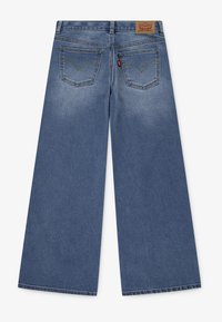 Wide-leg blue jeans made of denim, featuring two back pockets with a V-shaped design and a leather brand patch at the waistband.