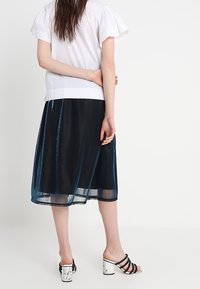 Vit topp med volangärmar, tillsammans med en genomskinlig midikjol i marinblått; skorna har en svart och vit marmorerad klack.