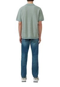 Polo en maille vert clair à manches courtes avec un motif texturé, associé à un jean bleu et des baskets blanches, vu de dos.