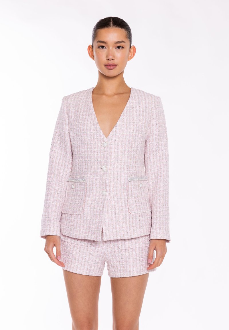 Vaaleanpunainen tweed-saketti, jossa syvä V-kaula-aukko, kaksi etutaskua ja napin yksityiskohtia. Yhdistyy samanlaista kangasta olevan shortsiparin kanssa.