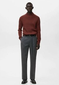 Geribbelde bordeauxrode coltrui gecombineerd met op maat gemaakte, hoog geribde grijze broek. Zwarte riem en gepolijste zwarte schoenen maken de look compleet.