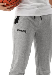 Grijze joggingbroek met zwarte accenten, gemaakt van zacht materiaal, voorzien van zijzakken en een zwart "SPALDING" logo op de linker dij.