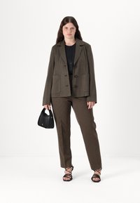 Brun rutete blazer og bukser sett, med notched krage, dobbelspent design, og en glatt tekstur. Svart håndveske i hånden.