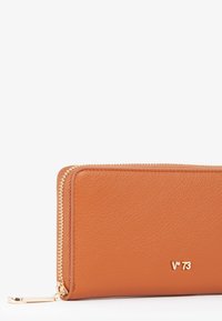 Portafoglio in pelle marrone con chiusura a zip, caratterizzato da una superficie testurizzata e accessori in tonalità oro. Logo visibile sulla parte anteriore.