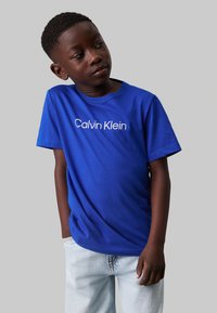 T-shirt a maniche corte blu con logo "Calvin Klein" bianco, abbinato a jeans in denim chiaro. Tessuto morbido e leggero.