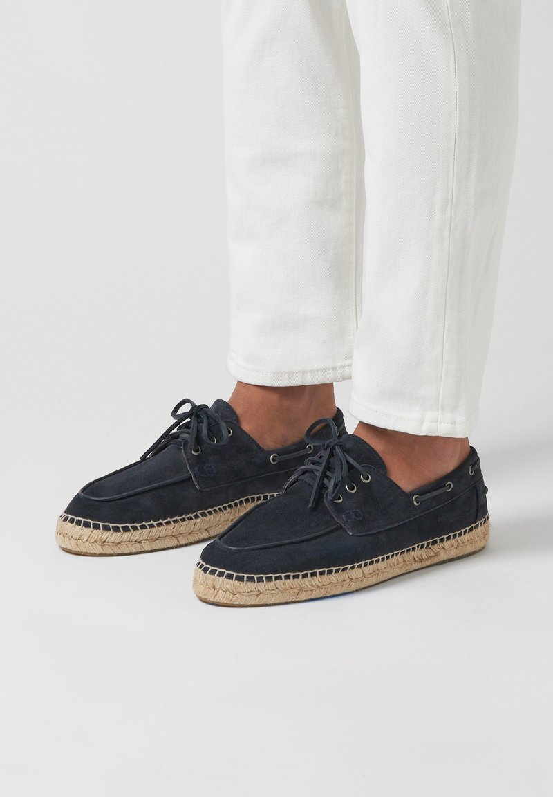 Chaussures en daim navy avec semelles en corde beige, à lacets et œillets métalliques. Présentent une texture lisse et une forme de bout arrondie.