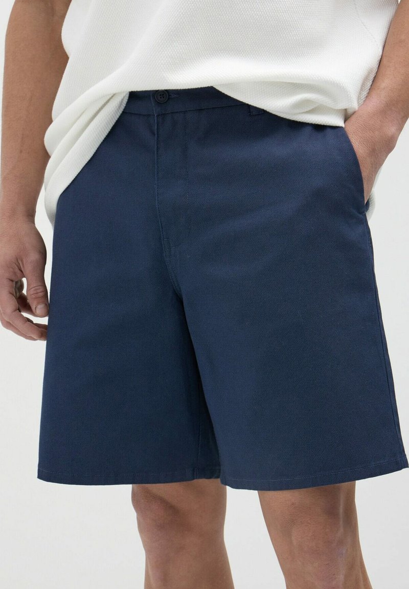 Pantaloni corti blu navy realizzati in tessuto testurizzato, con chiusura a bottone e tasche laterali, dal taglio dritto e orlo.