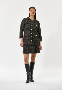 Schwarze und beiges karierter Tweed-Jacke mit goldenen Knöpfen, kombiniert mit einem passenden Rock und schwarzen kniehohen Stiefeln. Leichter, strukturierter Stoff.