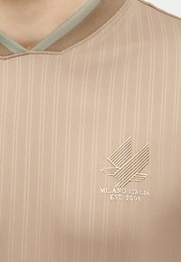 Μπεζ πουκάμισο με ρίγες και ριμπ λαιμόκοψη σε σχήμα V σε πράσινο και καφέ, με κεντημένο γεωμετρικό λογότυπο και κείμενο «MILANO ITALIA EST 2004».