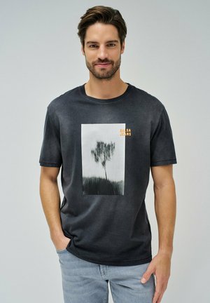 Camiseta negra de cuello redondo con un gráfico central en blanco y negro de un árbol; logo "SALSA JEANS" en naranja en la parte superior derecha. Material de algodón.