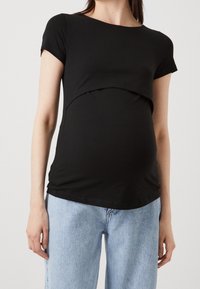 Svart graviditetstopp med korta ärmar, böjd framsidesdesign, mjukt jersey tyg, avslappnad passform, kombinerat med ljusblå jeans.