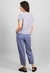 Top viola con motivo geometrico, abbinato a pantaloni azzurri a vestibilità larga e sandali neri, visto da dietro.