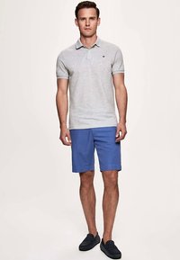 Grå poloskjorte med krage, kombinert med blå shorts. Skjorten har korte ermer og en liten logo på brystet. Shortsen er knelang.