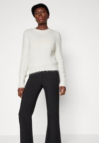 Maglione bianco пухoso con maniche lunghe, scollatura rotonda e vestibilità rilassata, abbinato a pantaloni neri aderenti. Fondo semplice.