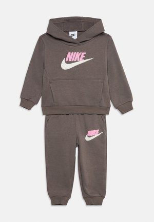 Παιδική καφέ φόρμα Nike με ροζ και λευκό λογότυπο, που περιλαμβάνει φούτερ με κουκούλα και ταιριαστό παντελόνι με ελαστικά μανσέτα.