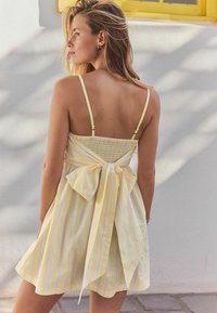 Gul och vit randig klänning med en figurnära bodice, smockad bak och en stor rosett vid midjan, med tunna justerbara axelband.
