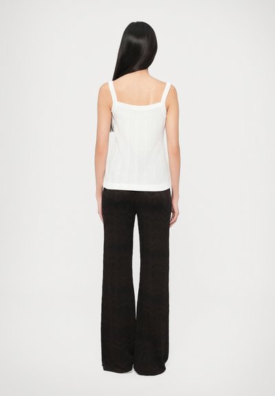 Λευκό πλεκτό τοπ με λεπτές τιράντες, με υφή ζιγκ-ζαγκ, συνδυασμένο με μαύρο, φαρδύ παντελόνι με σχέδιο.