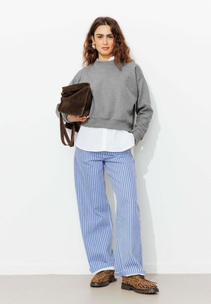 Sweatshirt gris court, chemise blanche en dessous, pantalon large rayé bleu et blanc, sac en daim brun et bottines en imprimé léopard.