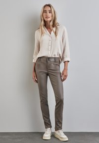 Beige, knappad skjorta med en texturerad tyg, kombinerad med slim-fit olivgröna byxor. Skorna är vita med beige detaljer.