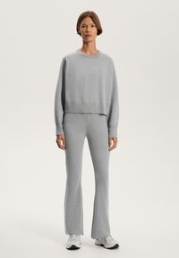 Grauer, verkürzter Sweatshirt mit langen Ärmeln und geripptem Saum, kombiniert mit passenden, ausgestellten Hosen aus weichem Material. Legere, sportliche Schuhe.