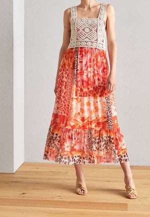 Kvinde iført ærmeløs hæklet top og orange patchwork midi nederdel med blomster- og dyreprint samt beige hælede sandaler.