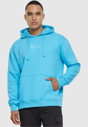 Lysblå pullover hoodie lavet af blødt stof, med en frontkangaroo lomme og et broderet logo på brystet.