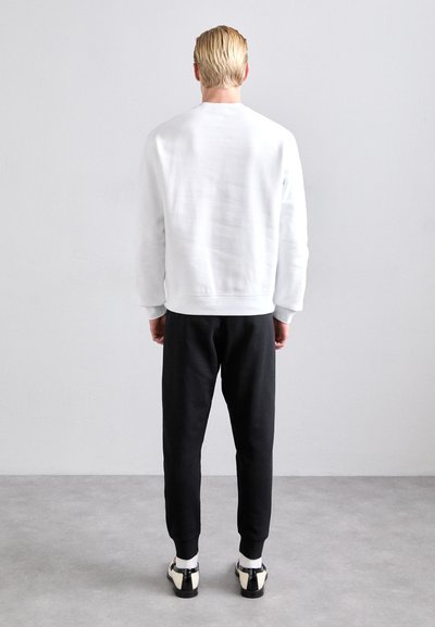 Hvid sweatshirt med rund hals, parret med sorte tætsiddende joggers, og afsluttet med sort-hvide sko. Minimalistisk design.