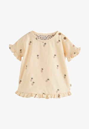 Persikinės spalvos medvilnės palaidinė su trumpomis volanų rankovėmis, papuošta ananasų siuvinėtomis detalėmis ir leopardų rašto pamušalu. Du mediniai mygtukai ant peties.