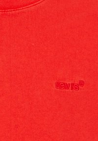 Tessuto rosso con un piccolo logo Levi's in rilievo ricamato vicino al lato in basso a destra dell'area visibile.