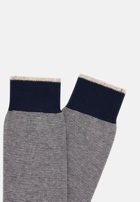 Námořnické a krémové pruhované ponožky s žebrovaným námořnickým lemem, měkkou texturou látky a klasickým designem. Hladký povrch s rovnoměrným šitím.