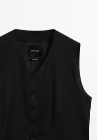 Svart ärmlös väst med V-ringning, featuring sex knappar fram, sidsömmar och en slät textur. Etiketten säger "Massimo Dutti."